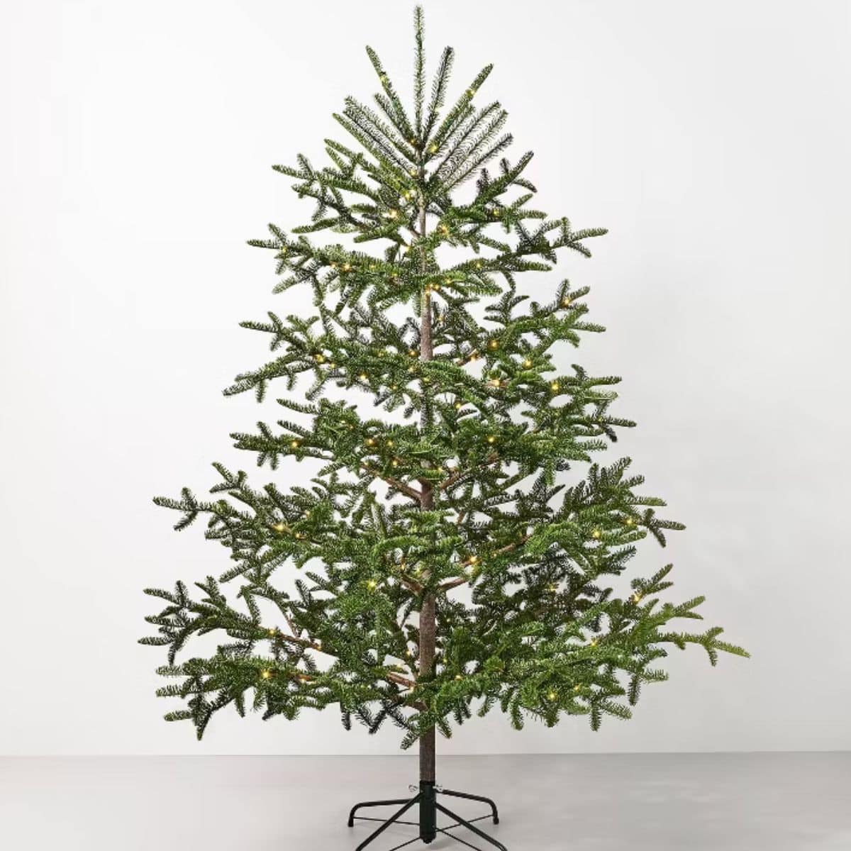 Pre-lit artificial spruce Christmas tree with warm white lights and realistic branches, displayed on a black metal stand.
