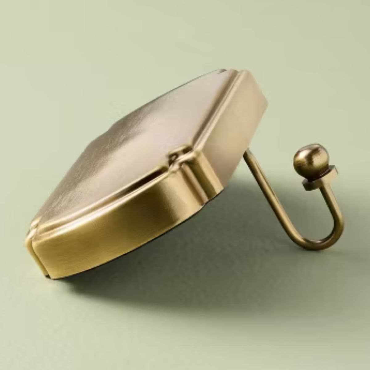 Gold metal stocking holder with a geometric base and curved hook, designed to hang Christmas stockings from a mantel or shelf.