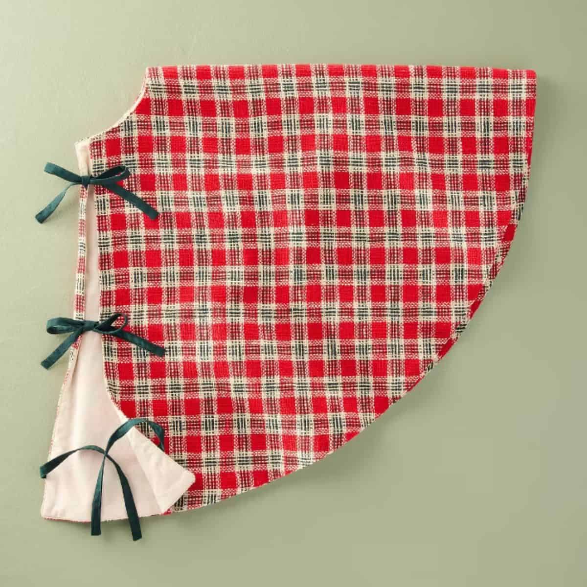Red and white plaid Christmas tree skirt with green ribbon ties and a soft white lining, styled in a classic vintage-inspired design.