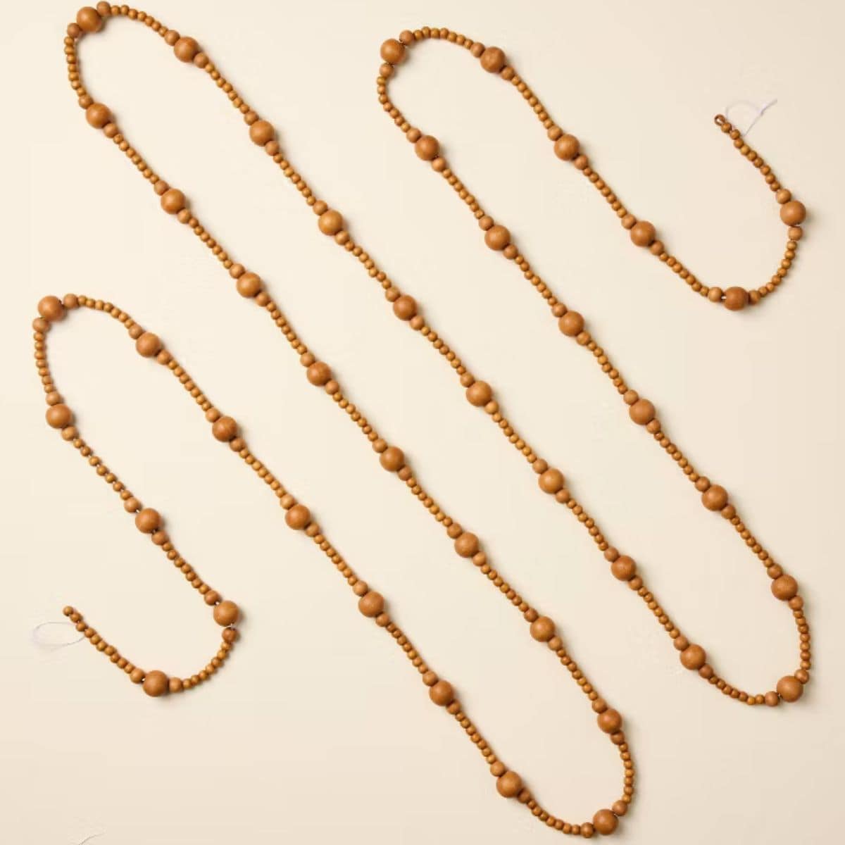 Long wooden bead Christmas garland featuring alternating small and large natural brown wood beads arranged in loose loops on a cream background.
