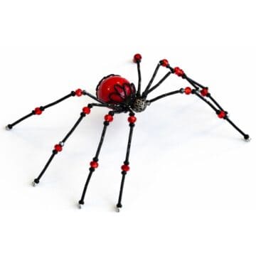 Handmade beaded spider with wire legs and red and black bead body displayed on a white background as a finished craft project.