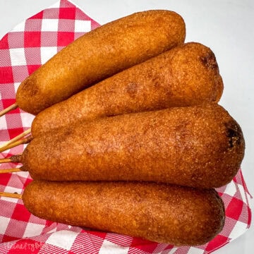 Four homemade corn dogs on a gingham napkin.