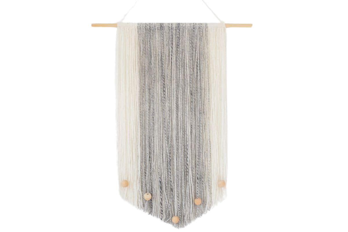 Modern yarn wall hanging with neutral-toned strands in gray and cream, accented with small wooden beads at the bottom and suspended from a wooden dowel.