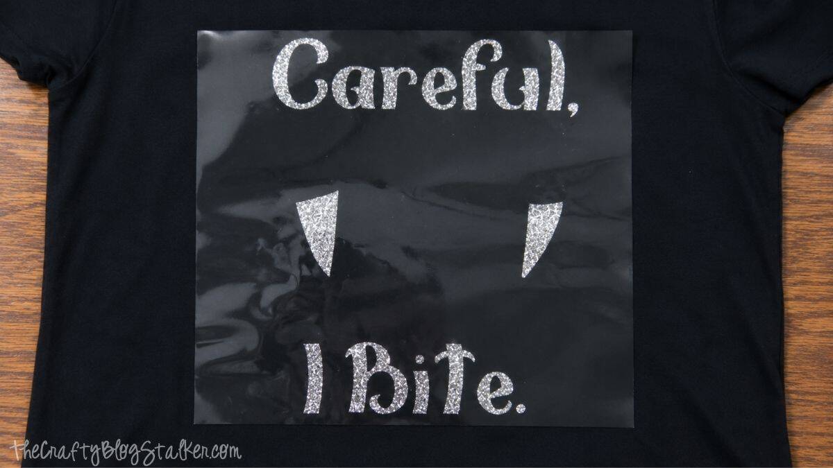 Silver glitter iron-on vinyl text and vampire fangs positioned on a black T-shirt for a layered Halloween design.