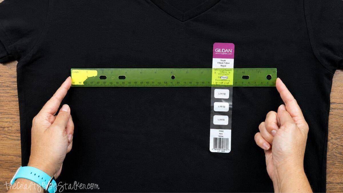 Hands holding a ruler across a black V-neck T-shirt to measure the width for placing a Halloween iron-on vinyl design.