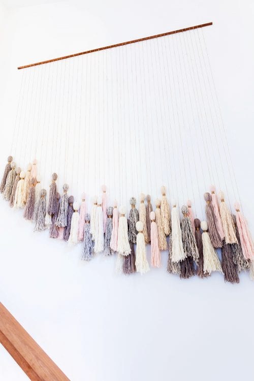 A large tassel wall hanging hung on a wall above a staircase.