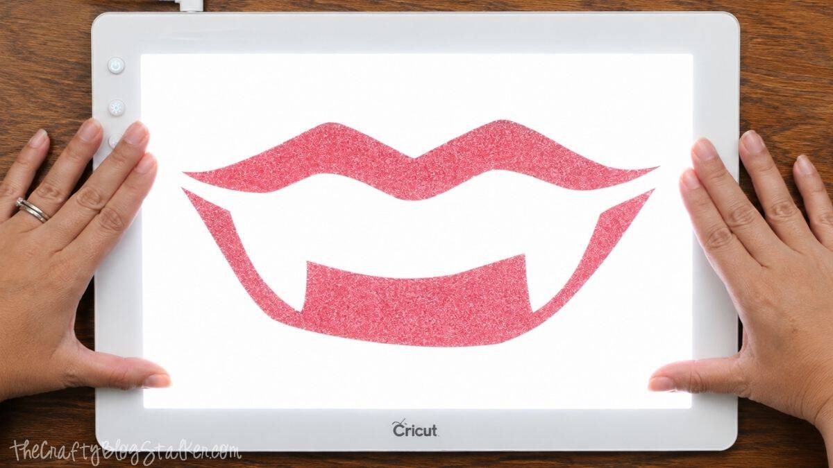 Red glitter vampire lips and fangs iron-on vinyl design displayed on a Cricut BrightPad for weeding.
