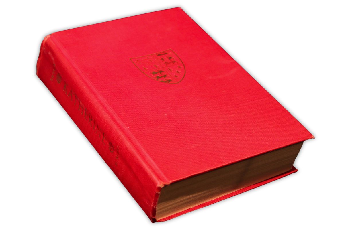 A red hardcover book with a gold embossed crest on the front cover and worn edges, closed and resting on a white background.