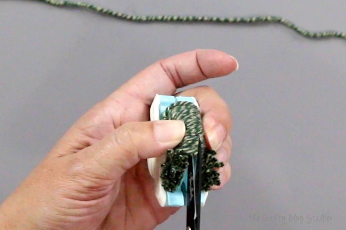 How to Make Pom Poms with the We R Memory Keepers Pom Pom Maker, a tutorial featured by top US craft blog, The Crafty Blog Stalker: cutting yarn