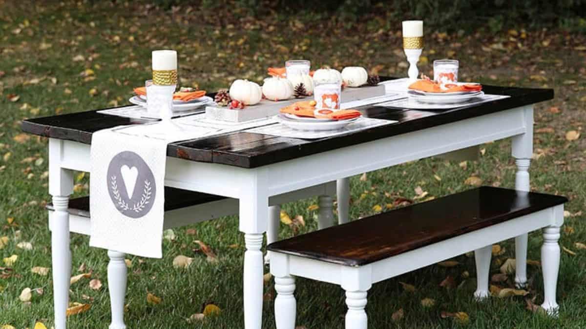 Outdoor Thanksgiving table with white benches, fall-themed place settings, mini white pumpkins, and candles arranged on a wooden table.