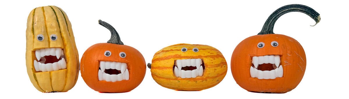 Four vampire pumpkins and gourds with googly eyes and plastic fangs lined up as playful Halloween decorations.