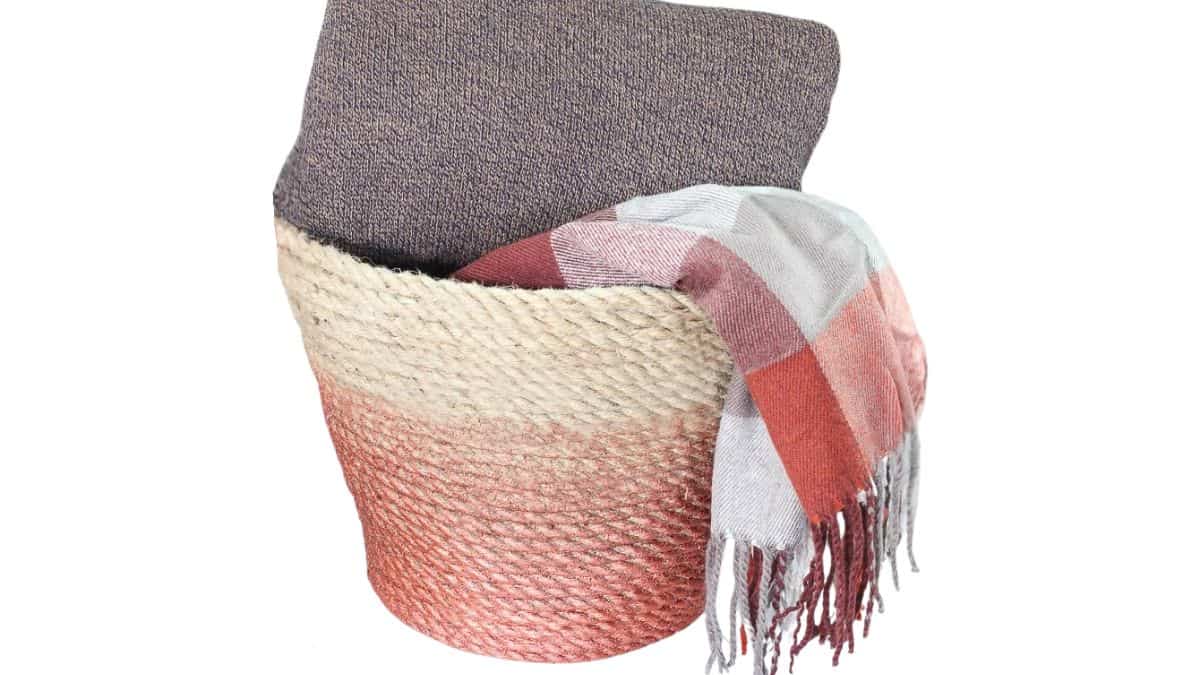 Woven rope throw basket with a folded blanket inside and a plaid scarf draped over the edge, styled as cozy home decor.