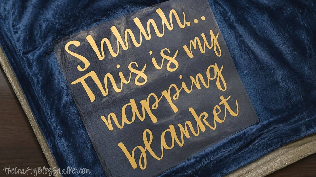 Gold iron-on vinyl with "Shhhh... This is my napping blanket" text placed on a blue plush blanket, ready for heat transfer application.