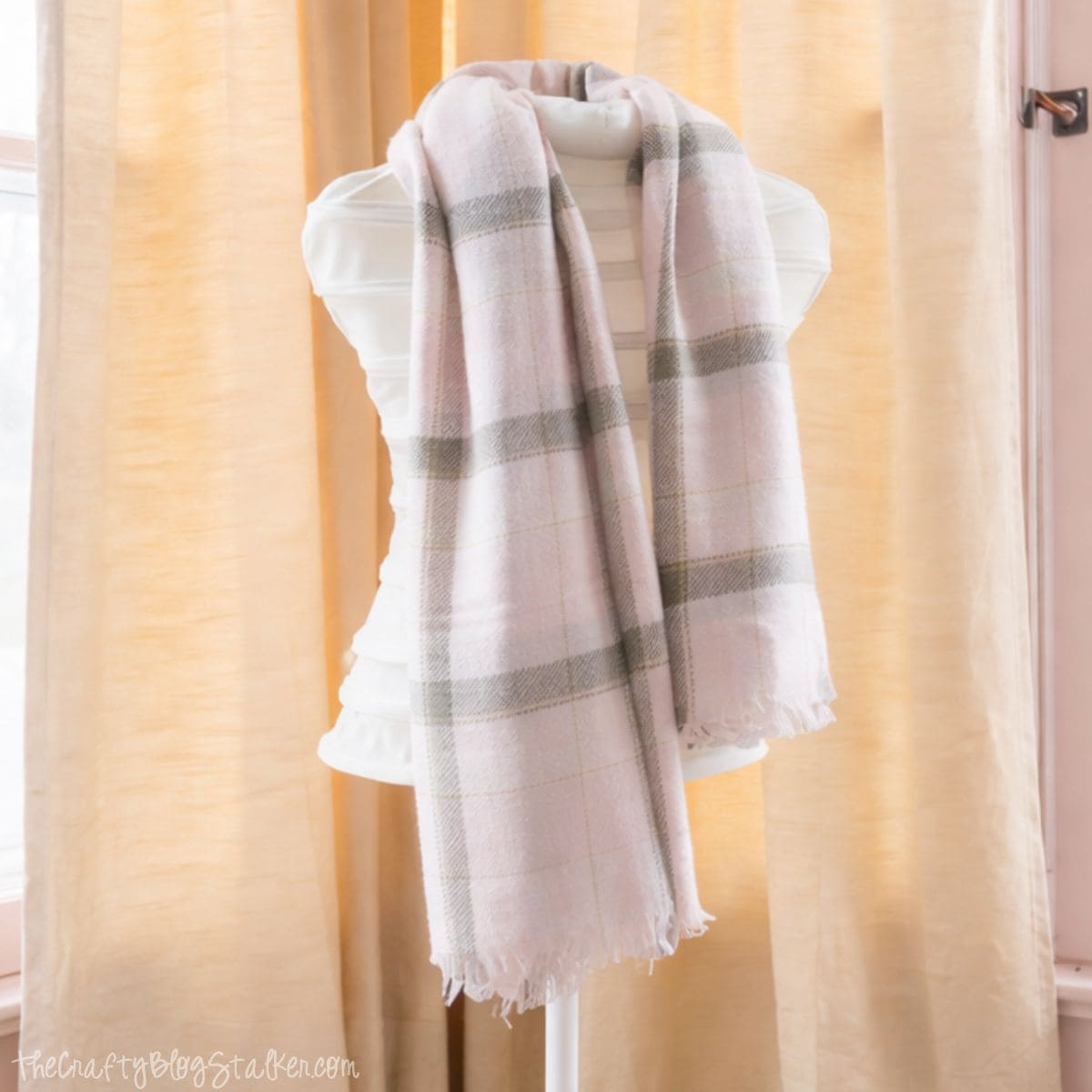 Dress form styled with a soft plaid scarf, positioned in front of sheer curtains in a bright, feminine bedroom.