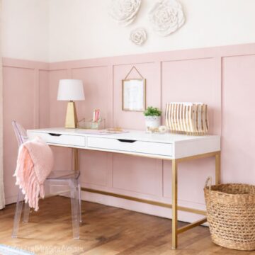 Girls bedroom desk setup with a modern writing desk, acrylic chair, table lamp, wall decor, woven basket, and organized stationery against paneled walls.
