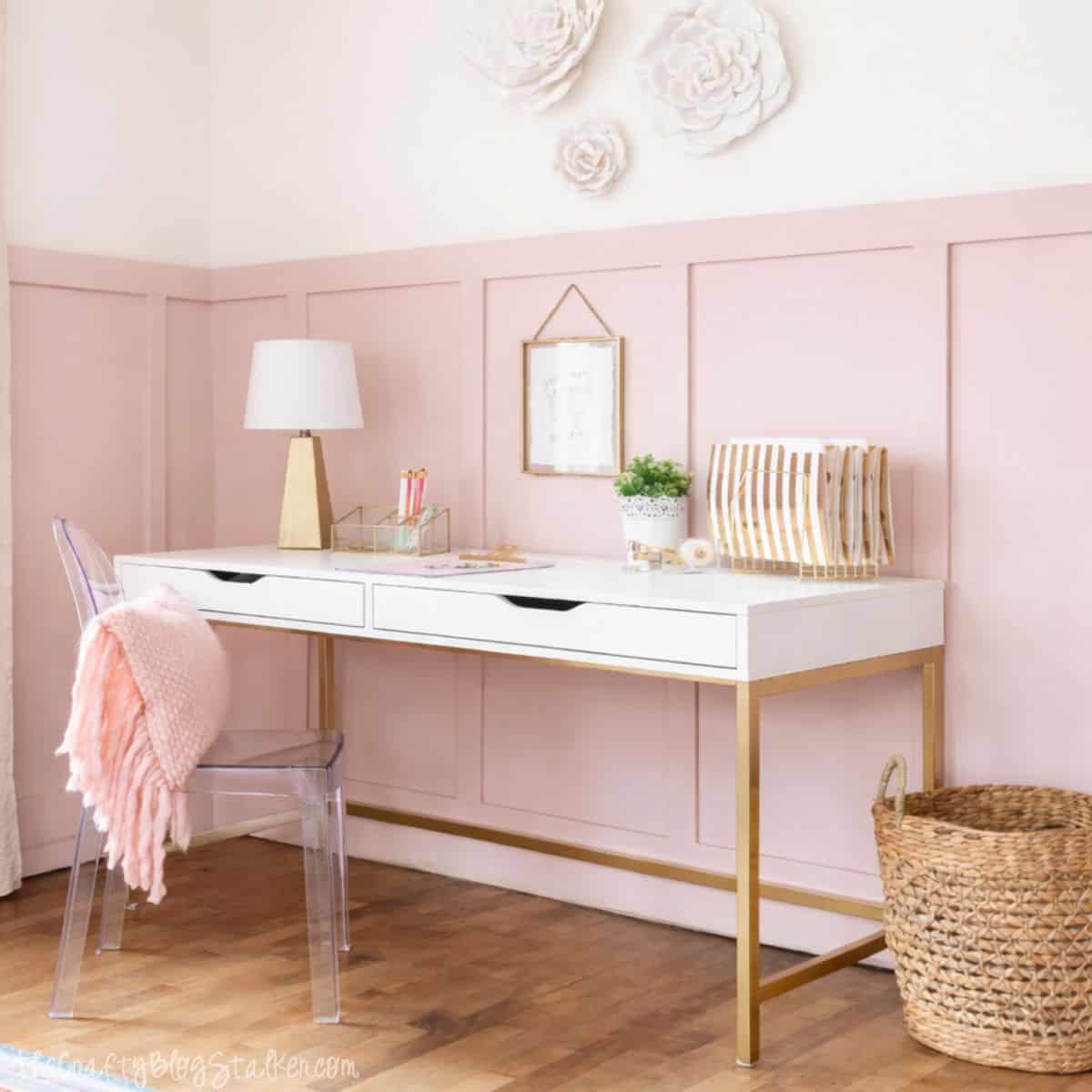 Girls bedroom desk setup with a modern writing desk, acrylic chair, table lamp, wall decor, woven basket, and organized stationery against paneled walls.