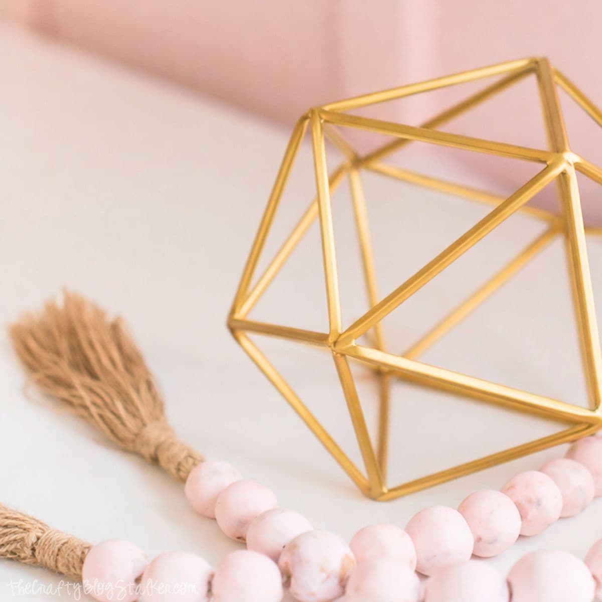 Geometric metal decor sits on a shelf beside a beaded garland with tassels, styled as a decorative accent in a bedroom vignette.