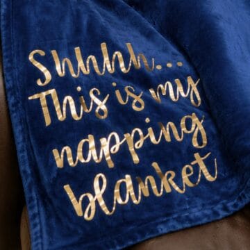 Close-up of a navy fleece blanket with metallic gold HTV lettering that reads, "Shhhh... This is my napping blanket," applied with heat transfer vinyl.