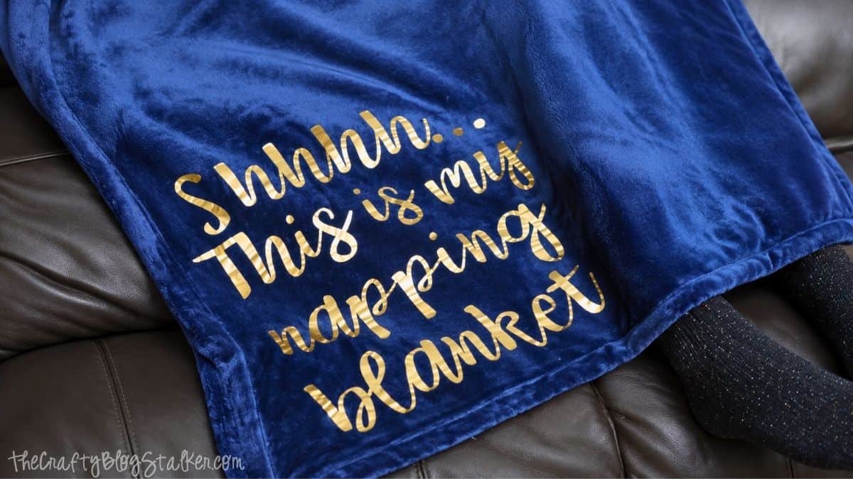 Soft navy blue blanket with gold lettering that reads "Shhhh... This is my napping blanket," draped over a surface, showcasing a cozy and relaxing vibe.