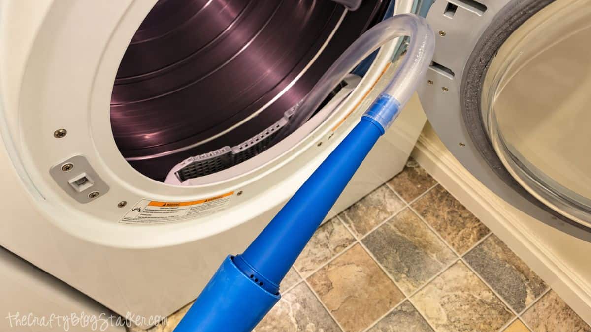 Flexible vacuum hose inserted into an open dryer to clean lint and debris from the dryer vent area.