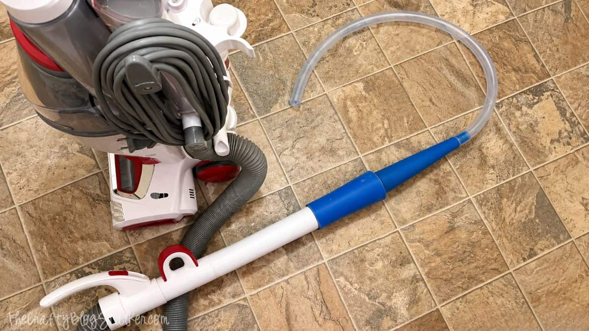Vacuum with a long flexible dryer vent cleaning hose attachment laid out on a tile floor.