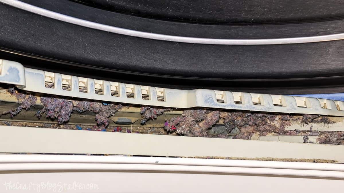 Heavy lint and debris buildup inside the dryer lint trap compartment beneath the drum.