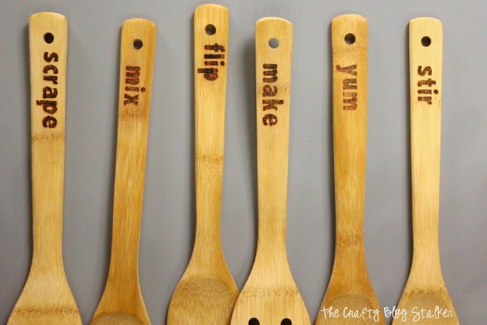 Wood burned spoons that read "Scrape, Mix, Flip, Make, Yum, and Stir".