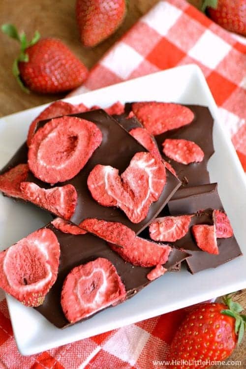 chunks of strawberry dark chocolate bark on a white plate with strawberries