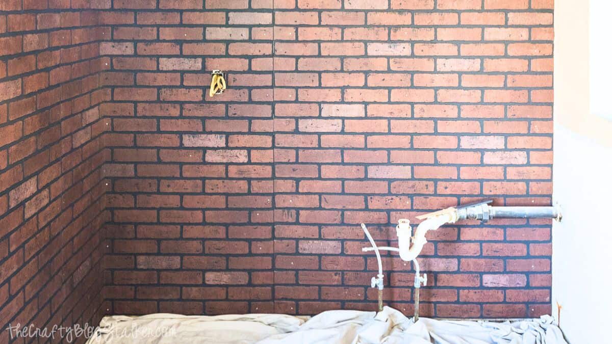Faux brick wall installed on an interior room wall, showing realistic brick pattern around exposed plumbing and electrical outlets.