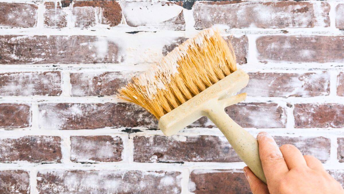 Using a masonry brush to apply joint compound over a faux brick wall, softening edges and creating a weathered brick texture.