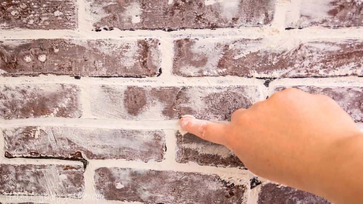 Finger smoothing joint compound between faux bricks, shaping mortar lines for a realistic brick wall finish.