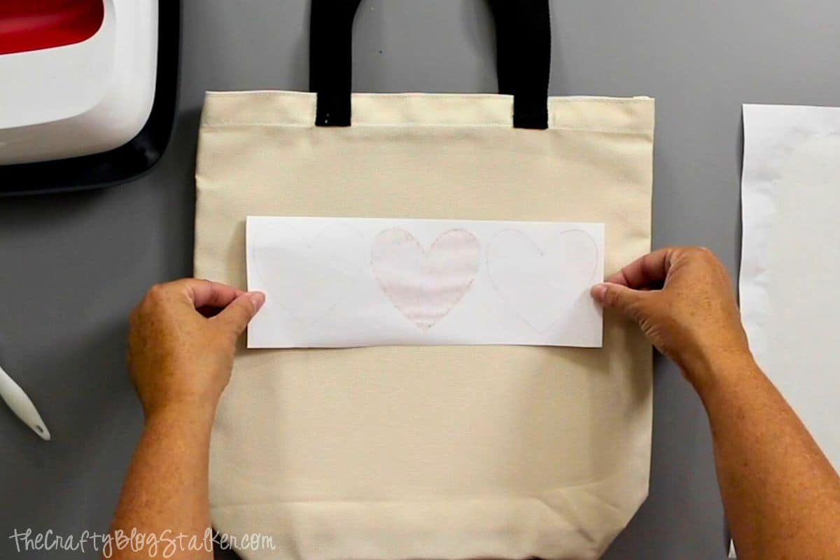 Centering the face-down  drawn design on the tote bag.