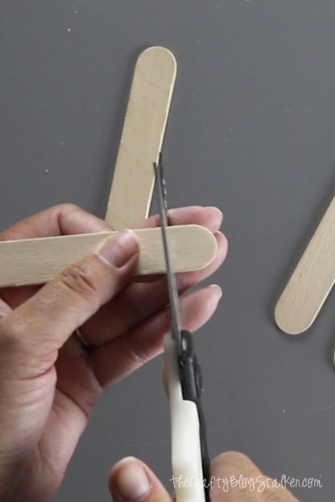 cutting off the curved edges of popsicle sticks with a pair of heavy duty scissors