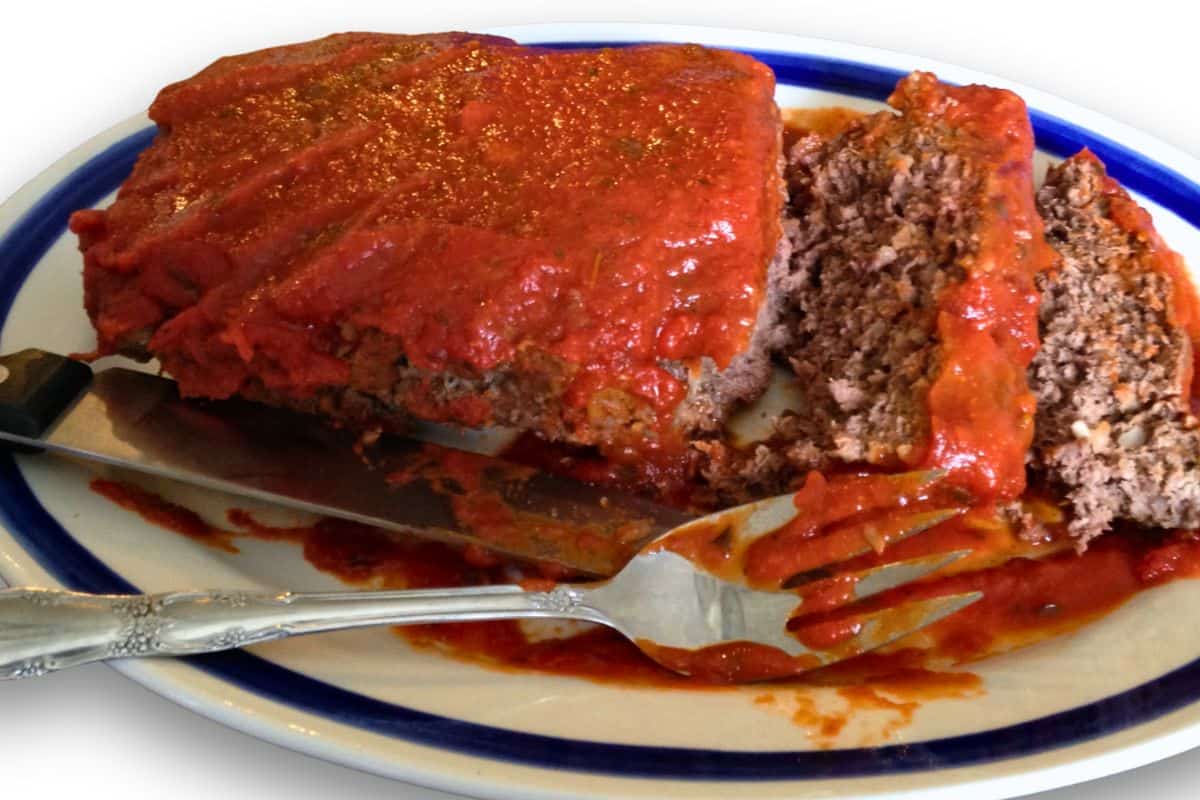 Sliced meatloaf on a white plate with a fork and knife.