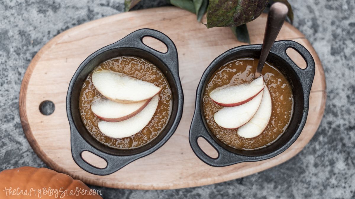 Two small black bowls filled with pumpkin applesauce, each topped with thinly sliced apples, placed on a wooden board.
