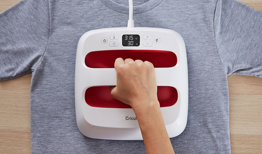 A Cricut EasyPress applying heat to a gray t-shirt.