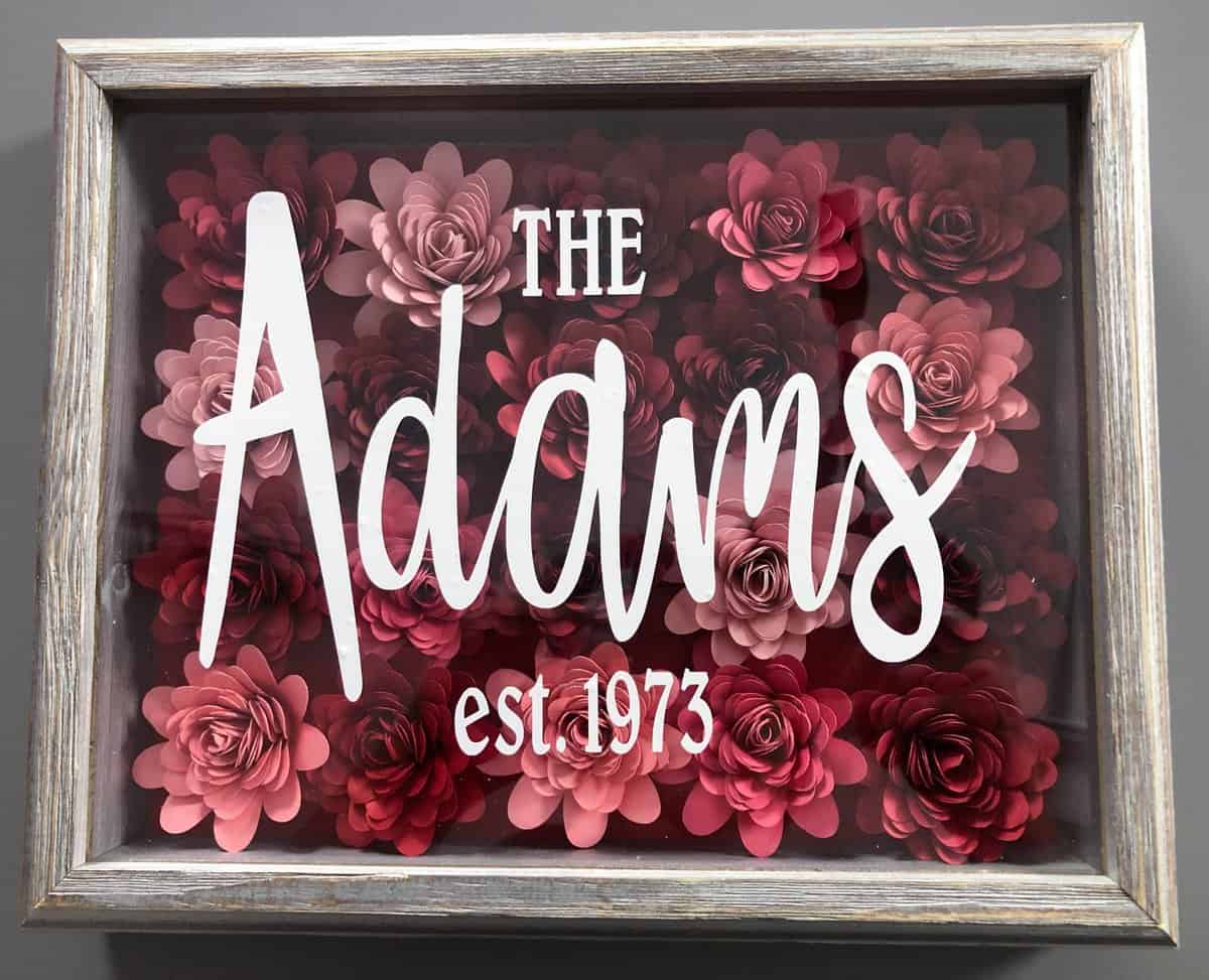 red and pink rolled flowers in a frame with "The Adams est. 1973" in white vinyl on the front.