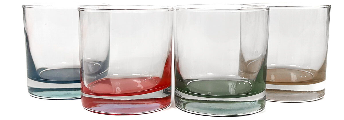 Set of four clear glass tumblers with colored bases in blue, red, green, and tan arranged in a row on a white background.