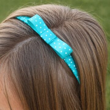 Close-up of a teal polka dot ribbon headband with a bow worn in a child’s hair.