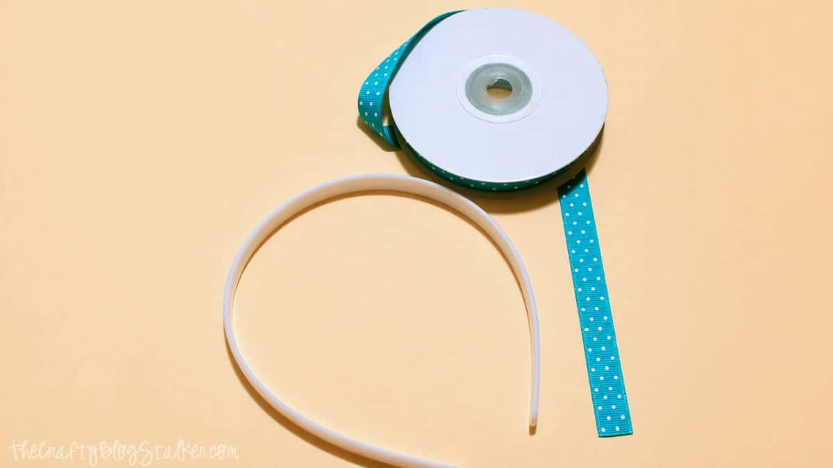 Plastic headband and roll of ribbon with white dots laid out on a plain background.