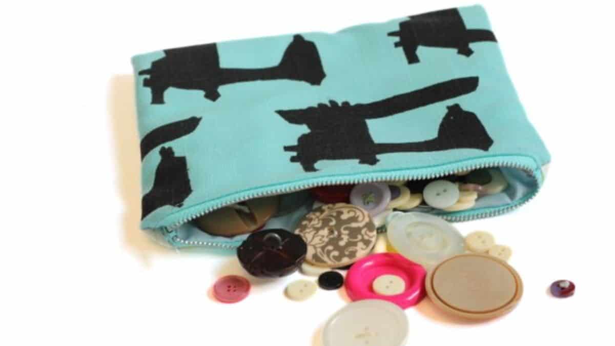 Handmade zippered fabric pouch with a bold pattern, partially open and filled with assorted buttons spilling out onto the surface.