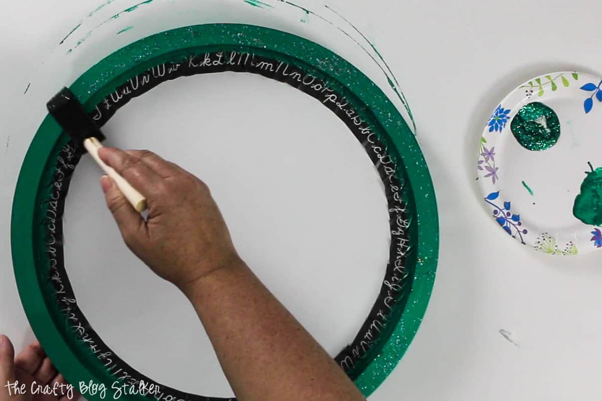 Painting green glitter onto the frame of the circle sign.