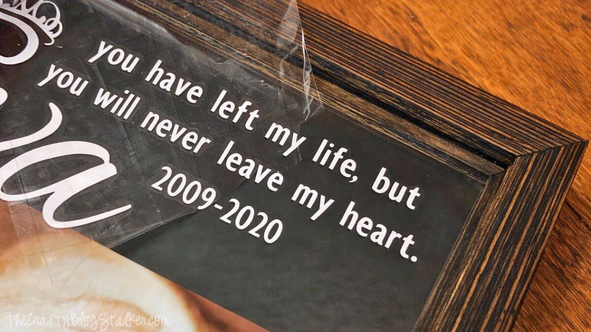 Close-up of transfer tape being peeled from a vinyl memorial quote applied inside a wooden shadow box frame.