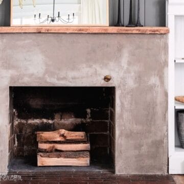 Concrete fireplace makeover with a smooth gray finish, natural wood mantel, stacked firewood, and styled built-in shelves on each side.