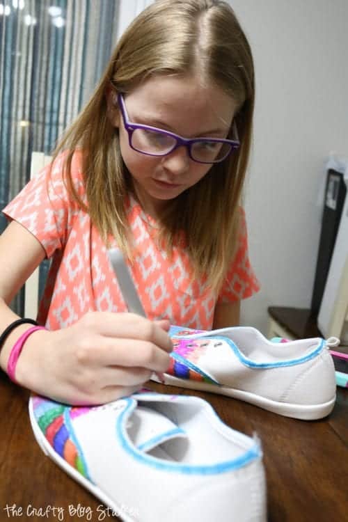 a girl coloring shoes with sharpie markers