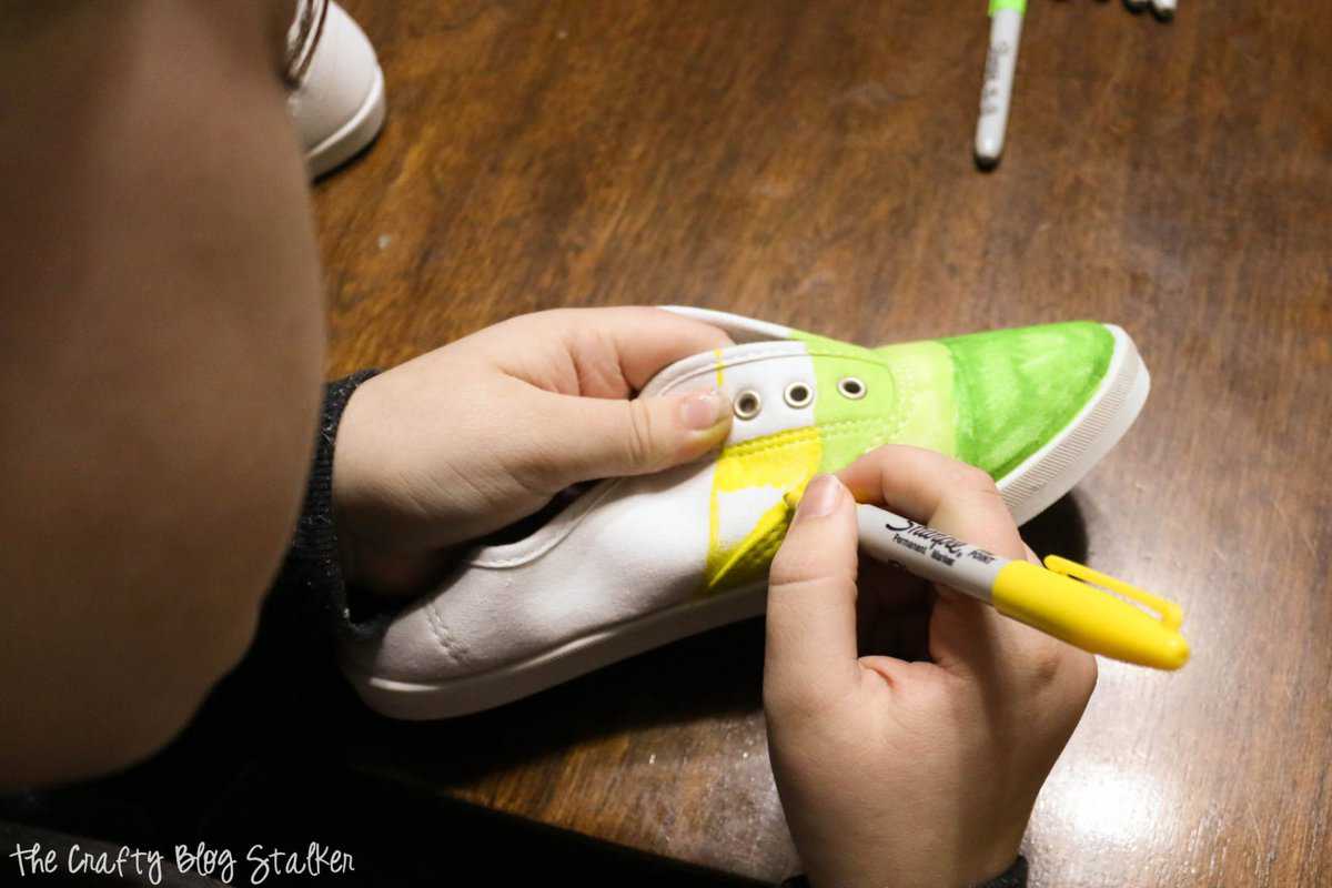 a girl coloring shoes with sharpie markers