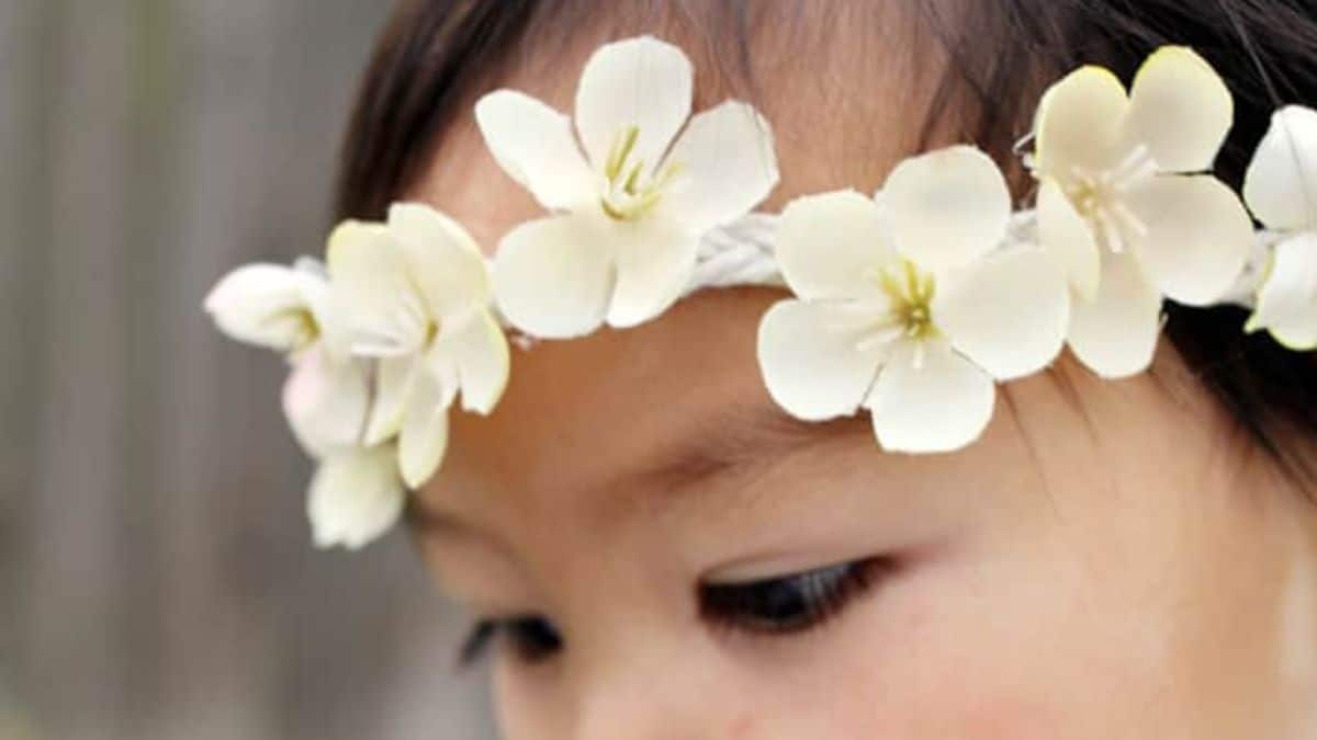Close-up of a child wearing a white floral headband with cream-colored flowers across the forehead.