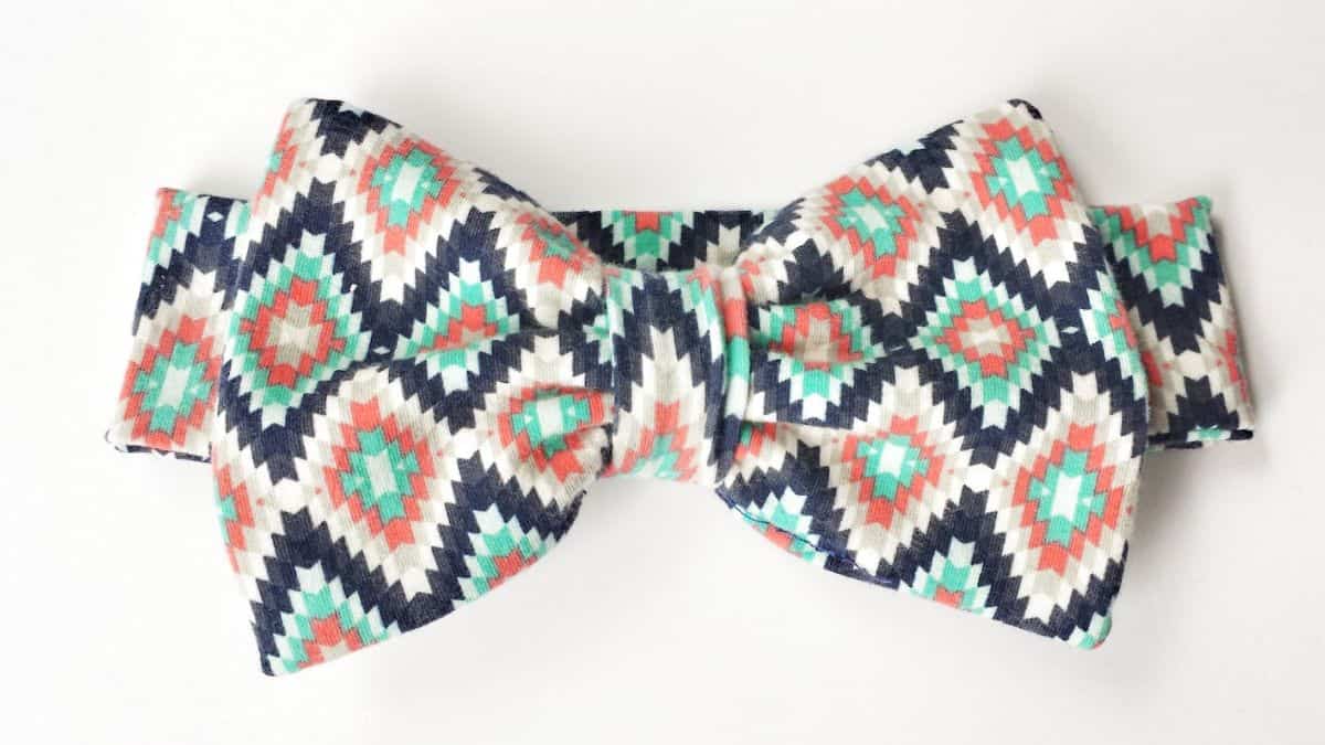 Patterned knit fabric bow headband with a colorful geometric print in coral, mint, navy, and cream on a white background.