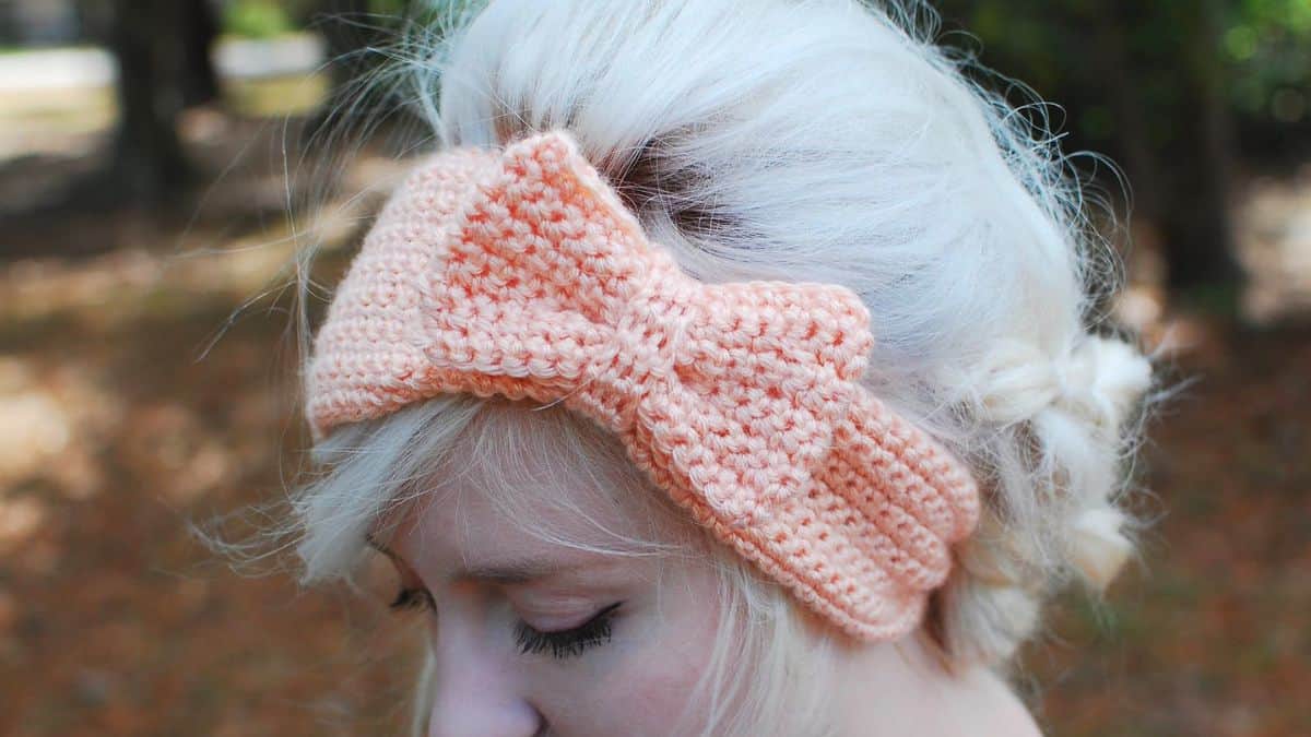 Woman wearing a soft pink crocheted bow headband with platinum blonde hair styled in a loose bun outdoors.