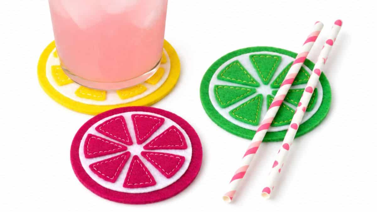 Colorful felt citrus slice coasters in pink, yellow, and green displayed with a pink drink and striped paper straws.